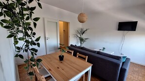 Un espace de vie moderne avec une table à manger en bois, un canapé gris foncé et un téléviseur fixé au mur.