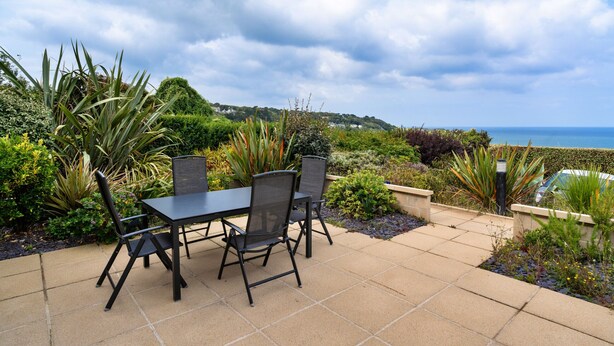 Eine Terrasse im Freien mit Tisch und Stühlen, umgeben von Pflanzen und Blick aufs Meer.