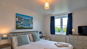 A neatly arranged bedroom with a bed, bedside tables, a TV, and a window with curtains. - Blue Horizon (St Ives)