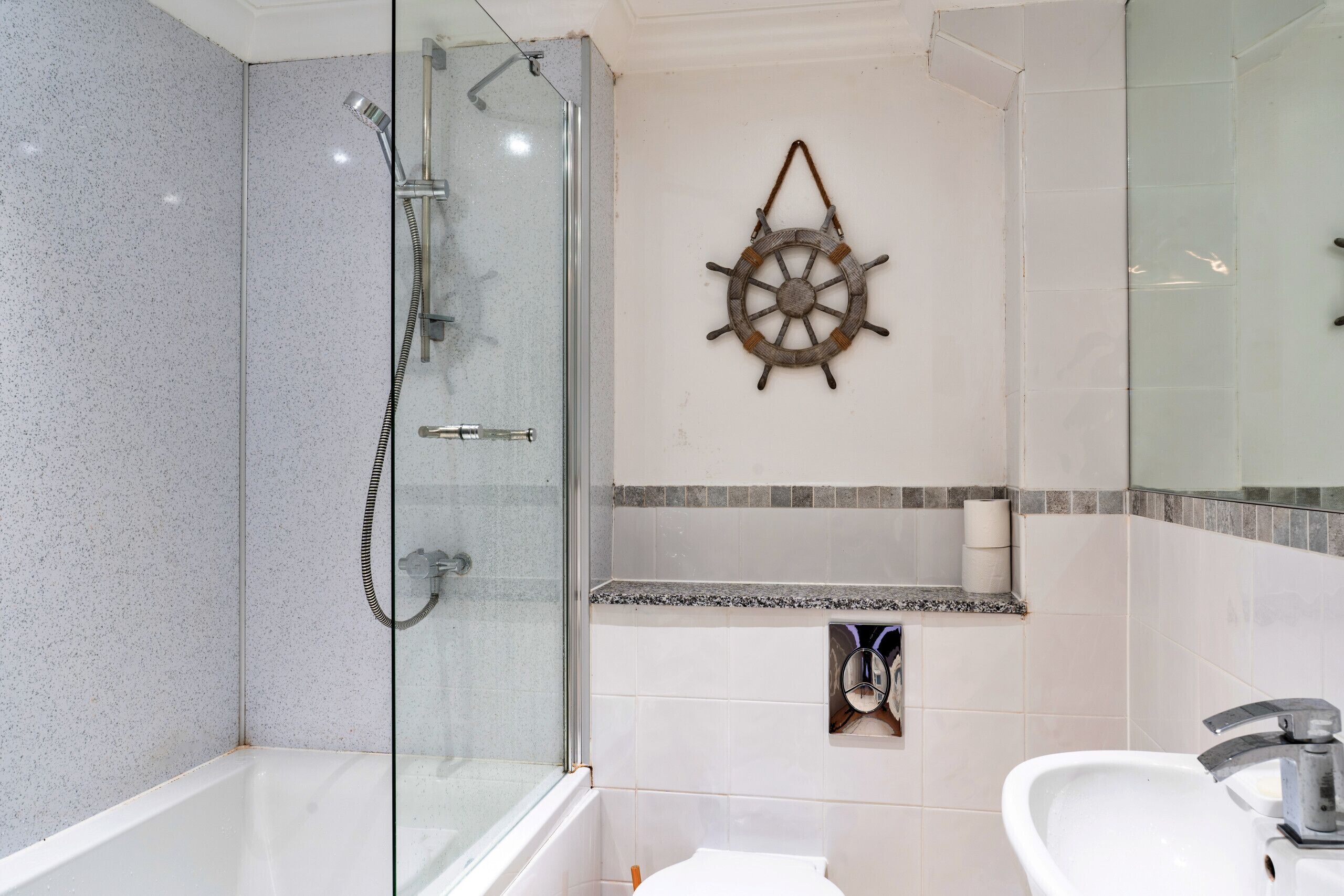 Une salle de bain avec une douche à parois de verre, une décoration en forme de roue de navire, un lavabo et des toilettes.