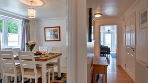 A dining area with a wooden table and white chairs, a colorful rug, and a painting on the wall. - Blue Horizon (St Ives)