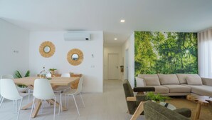Ett modernt vardagsrum med ett stort fönster, en soffa, ett soffbord och en matplats med ett träbord och vita stolar.