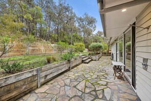 A stone patio with a table and chairs, surrounded by a wooden fence and vegetation.