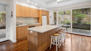 Una cucina moderna con mobili in legno, un'isola centrale con sgabelli e un'ampia porta scorrevole in vetro che dà su uno spazio esterno.