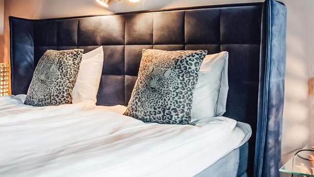 Un dormitorio moderno con cabecera capitonada, cama con ropa de cama blanca y almohadas de estampado de leopardo.