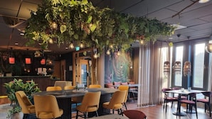 Restaurante con techos altos, plantas colgantes e iluminación moderna. Mesas y sillas dispuestas para comer.