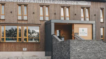 Ett spa-hotell med en träfasad, en entré i sten och en skylt som visar namnet och åren 2023–2024.
