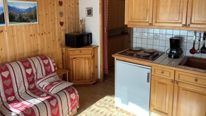 A cozy room with a wooden sofa, a small cabinet, a microwave, a refrigerator, and wooden cabinets.