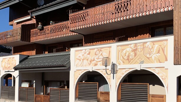 A traditional wooden building with balconies, arched doorways, and decorative wall panels.