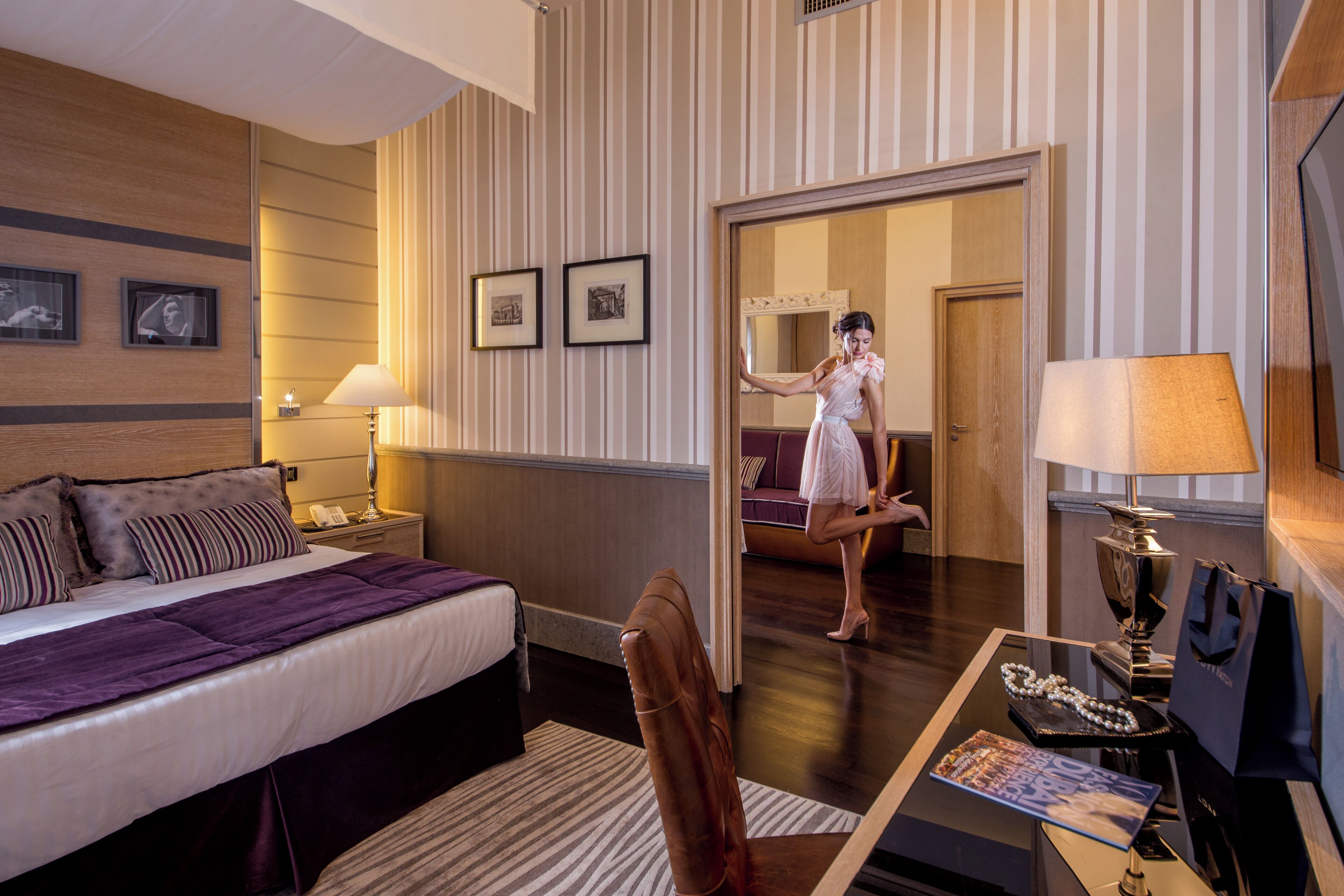 A hotel room with a bed, a desk, a chair, a mirror, and a door leading to another room.