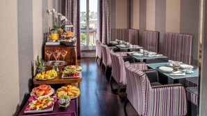 A dining area with striped booths, a buffet with fruits and desserts, and a view of the city through large windows. - The Inn at the Spanish Steps Luxury Collection - Spanish Steps Suites (Rome)