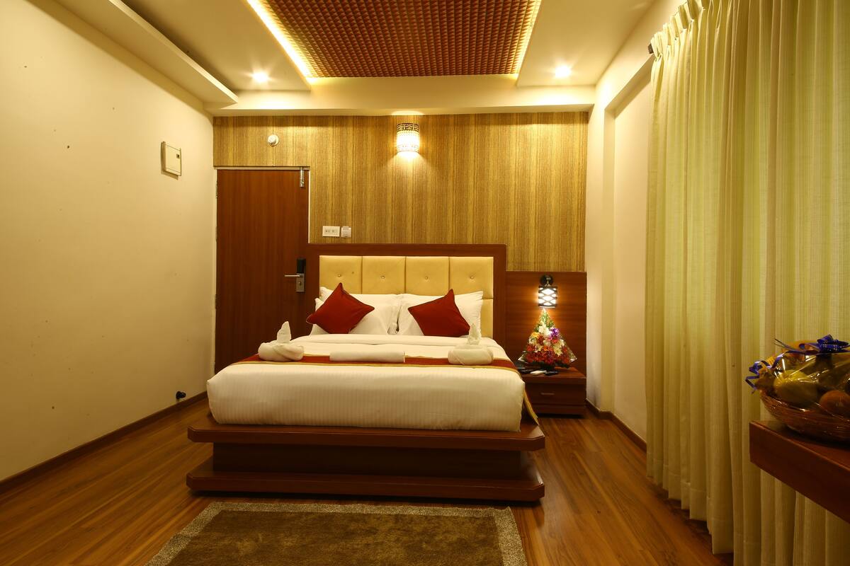 A hotel room with a large bed, wooden flooring, a nightstand, and a wall-mounted light fixture.