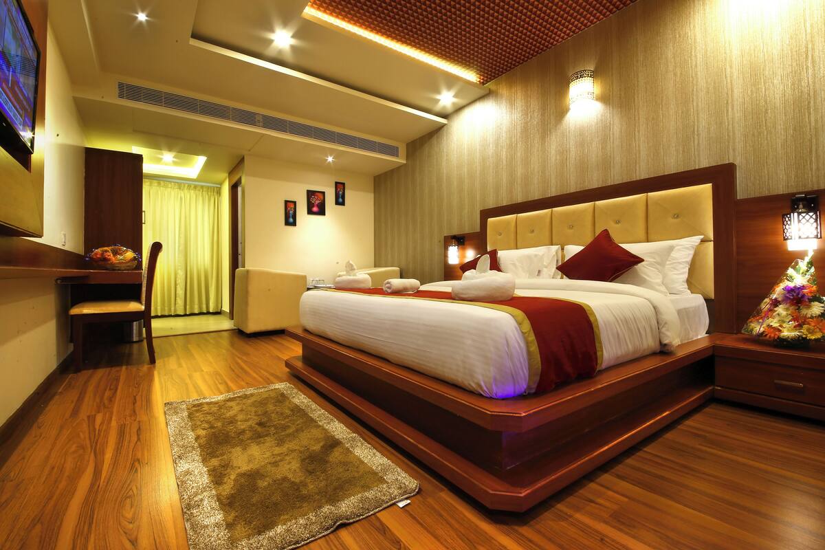 A hotel room with a large bed, wooden flooring, a small desk, and a chair.