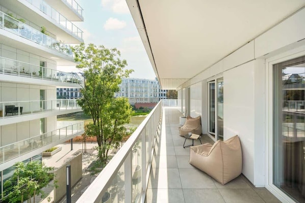 Un appartement moderne doté d’un balcon, de grandes fenêtres et offrant une vue sur d’autres immeubles.