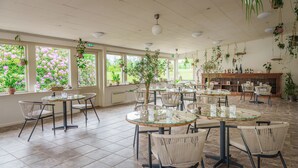 A spacious restaurant with round tables and chairs, large windows with views of pink flowers, and hanging plants. - Morup Mølle Kro (Bedsted)
