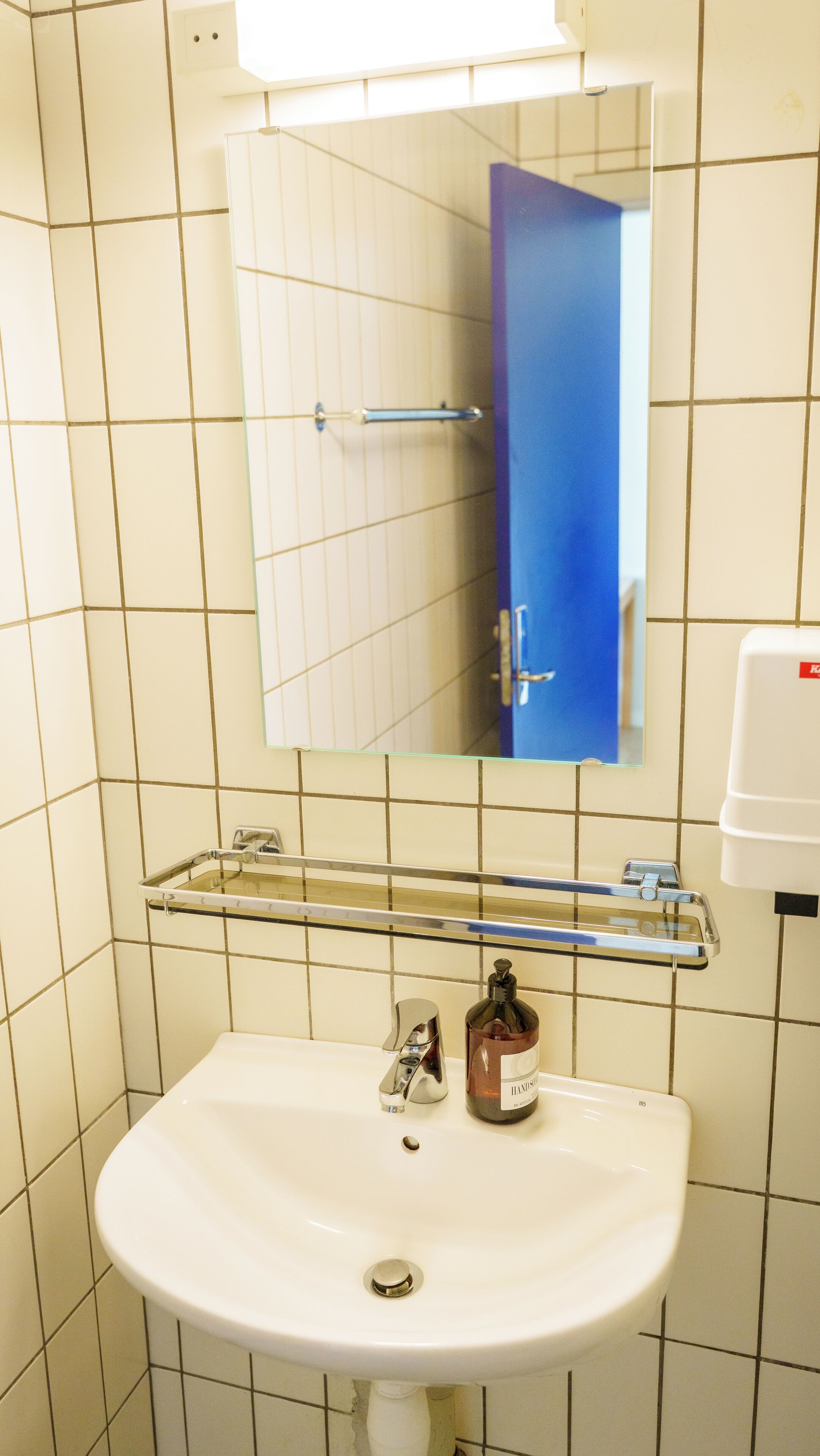 Un baño con lavamanos blanco, un espejo y una puerta azul.