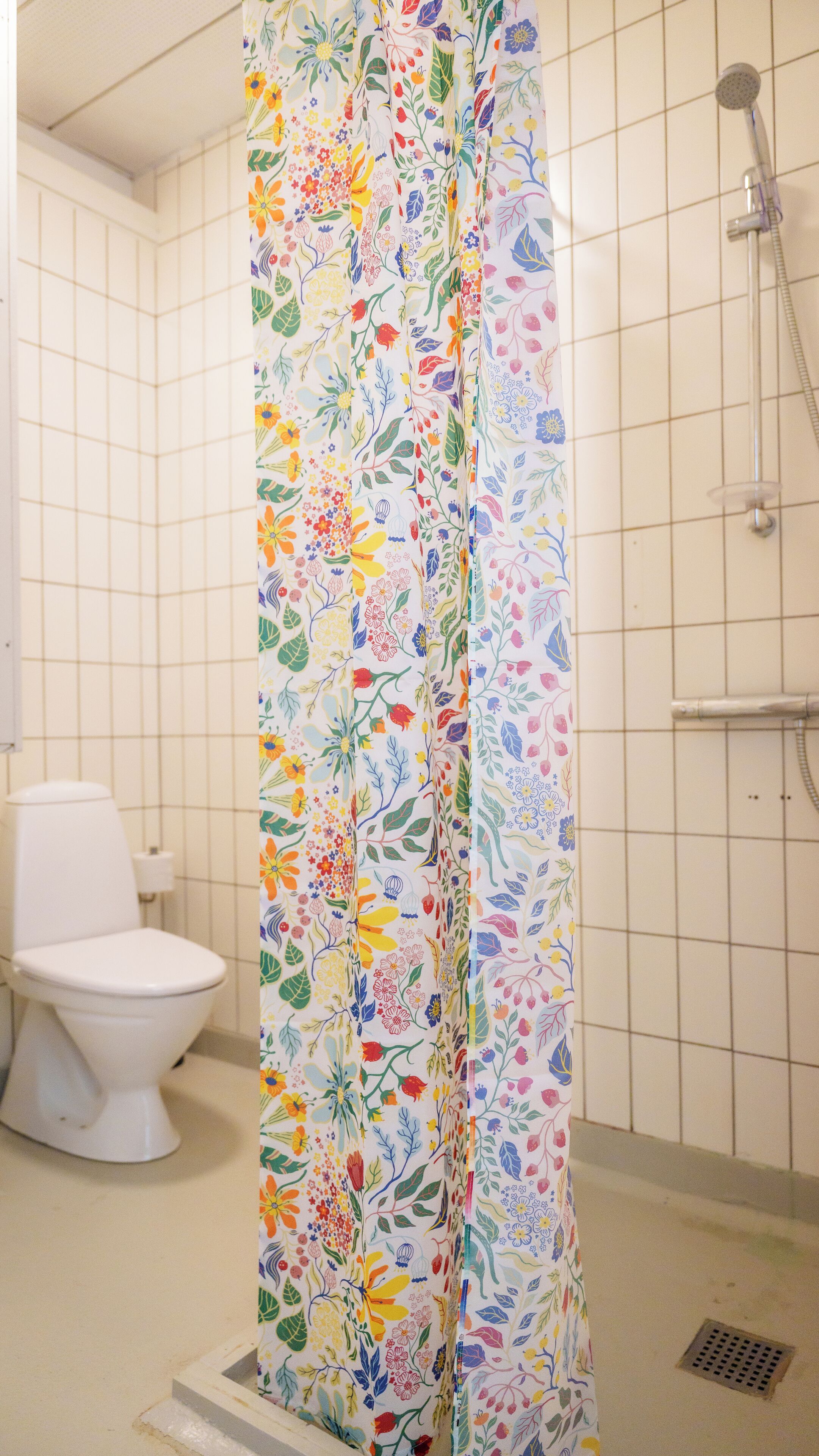 A bathroom with a shower curtain featuring a floral pattern, a toilet, and a showerhead.