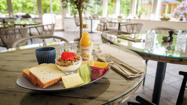 A breakfast setting with toast, yogurt with granola and a strawberry, cheese, meat, and a bottle of orange juice on a table. - Morup Mølle Kro (Bedsted)