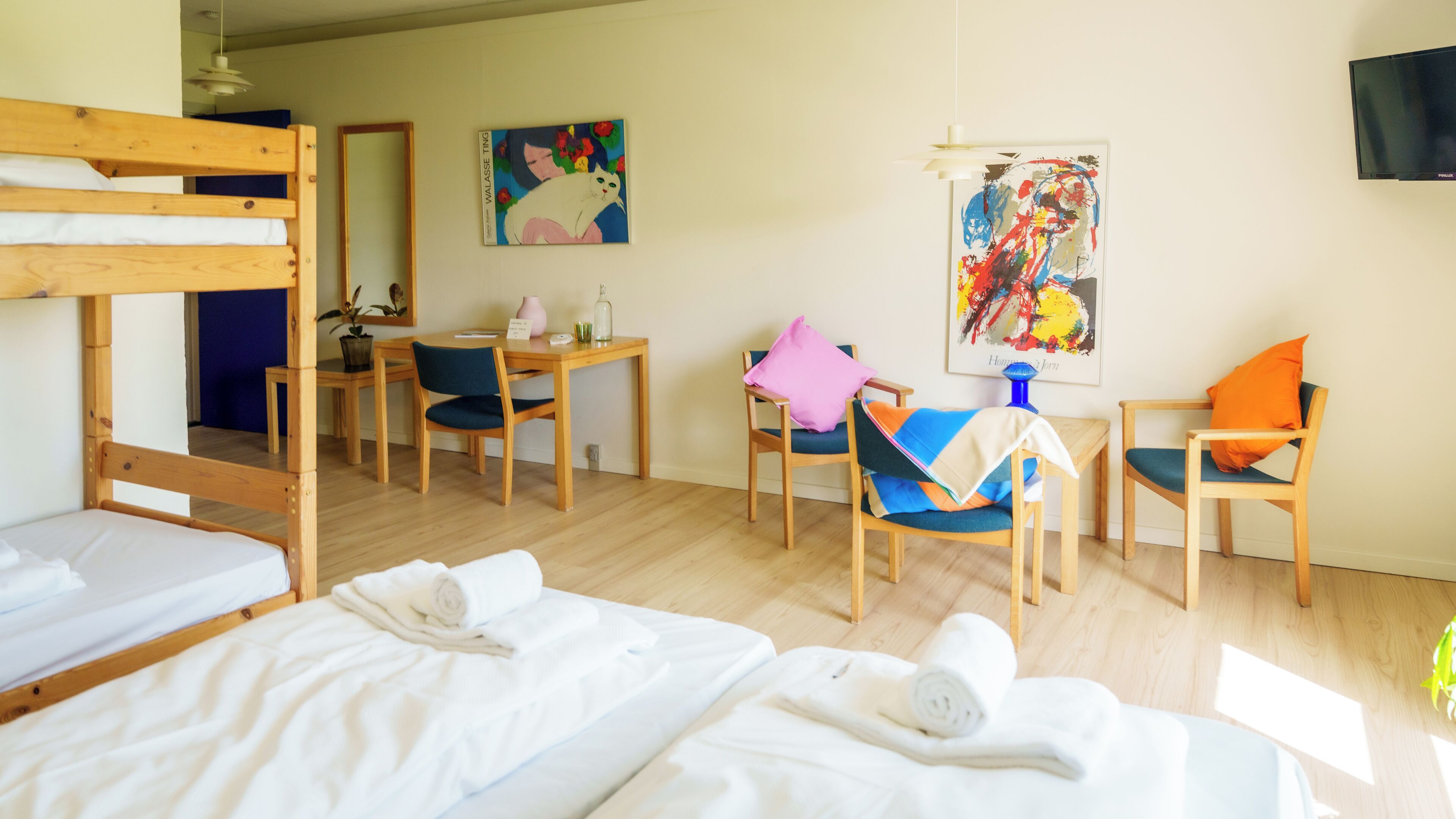 Una habitación de hotel con literas, un escritorio, sillas y obras de arte en las paredes.