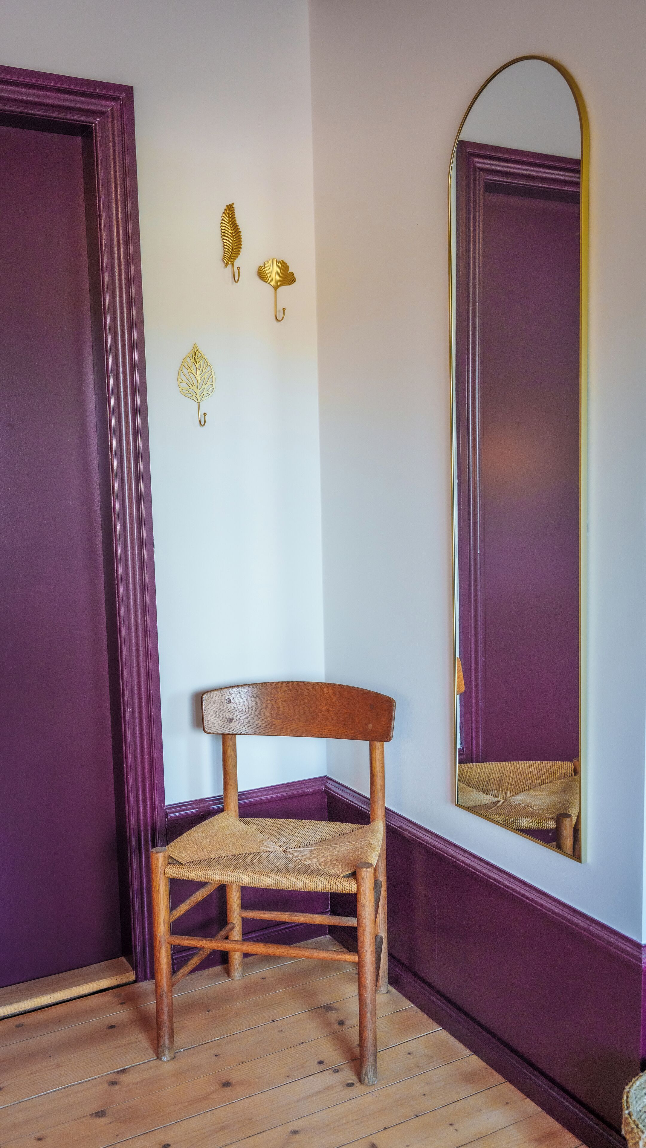 Una habitación de esquina con una silla de madera, un espejo y decoración en la pared.