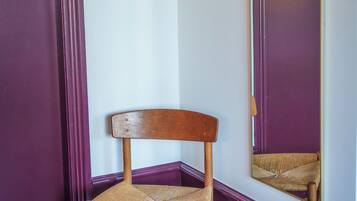 Una habitación de esquina con una silla de madera, un espejo y decoración en la pared.