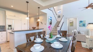 A spacious dining area with a wooden table set for four, surrounded by white cabinets and a kitchen in the background.