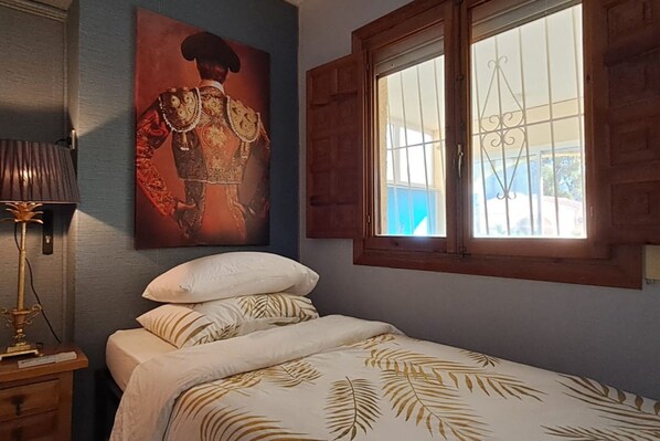 A bedroom with a bed, a nightstand, a lamp, a window with bars, and a painting on the wall. - Adults Only Exclusive Mediterranean Private Escape (San Fulgencio)