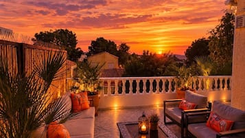 Un patio con mobiliario exterior, piso estampado y vistas al atardecer.