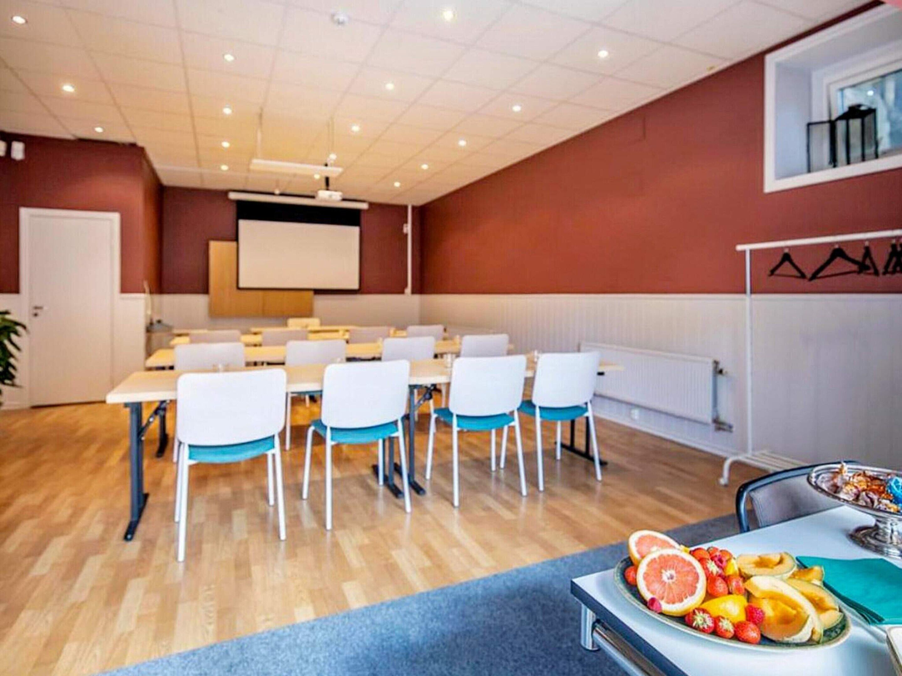 A conference room with white tables and chairs, a projector screen, and a fruit platter on the table.