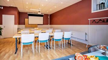 A conference room with white tables and chairs, a projector screen, and a fruit platter on the table.