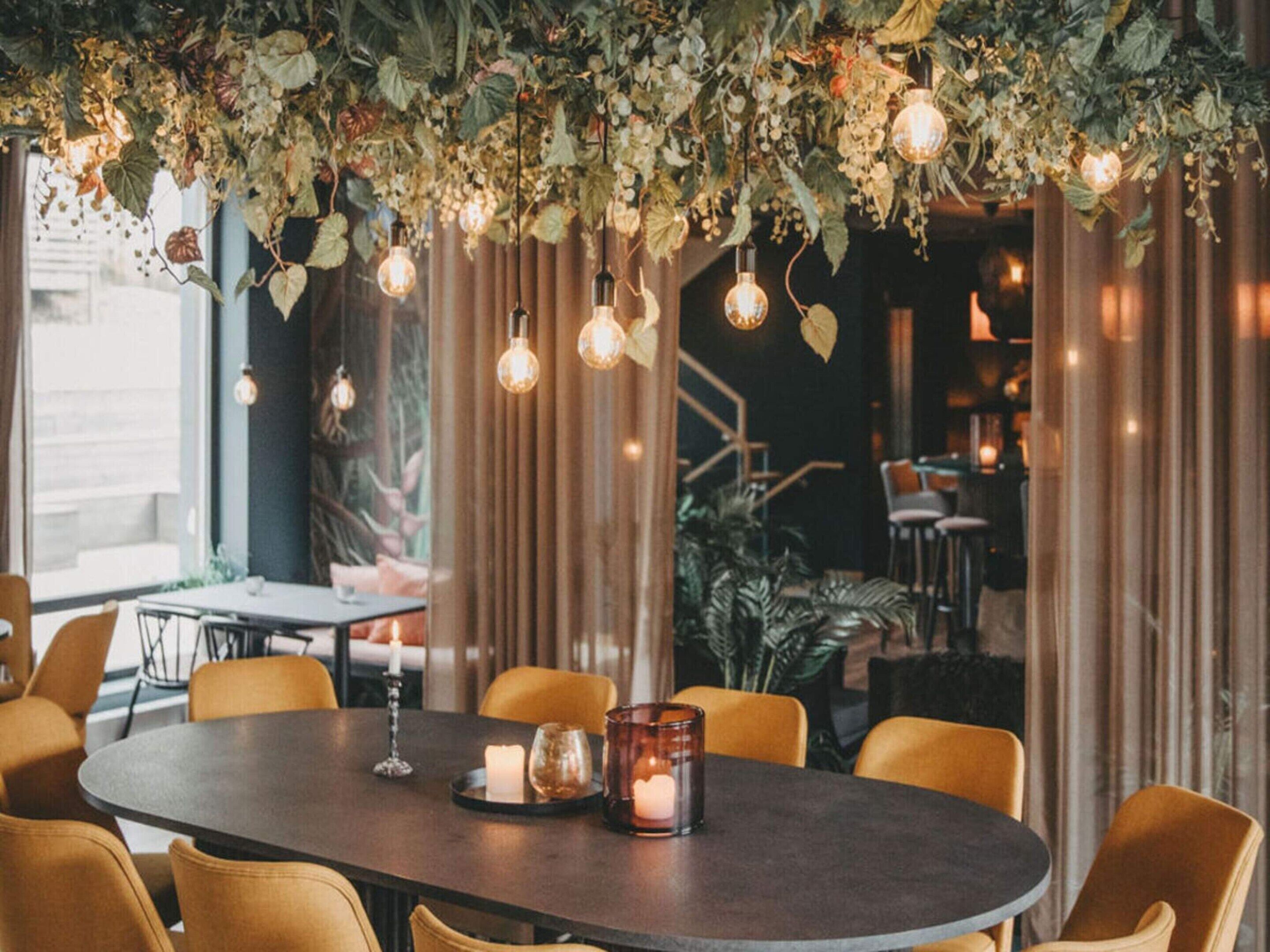 An indoor dining area with a round table, yellow chairs, hanging light bulbs, and a curtain backdrop.