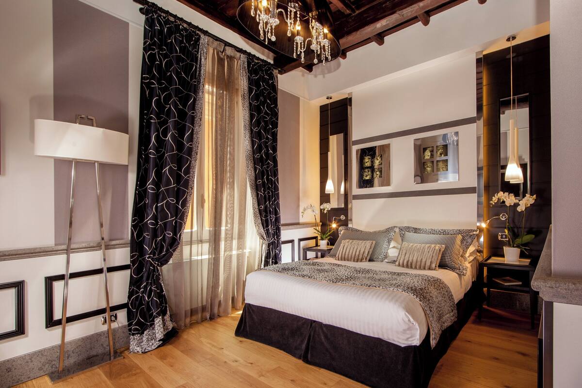 A bedroom with a large bed, a chandelier, a nightstand, and a mirror.