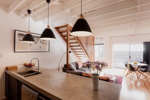 Een moderne keuken met een centraal eiland, hanglampen, een houten trap en een eethoek met uitzicht.