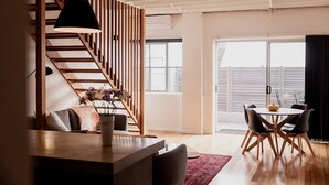A modern interior with a wooden staircase, a dining area with a round table and chairs, and large windows offering a view. - Urban Warehouse Retreat in West Hobart (West Hobart)