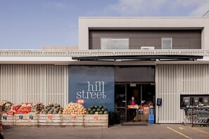 L’entrée d’une épicerie, avec une enseigne indiquant « Hill Street » et des produits frais exposés à l’extérieur.