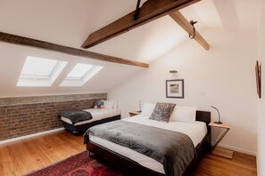Une chambre avec deux lits, des fenêtres de toit, un mur en briques et une poutre en bois au plafond.