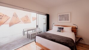 A modern bedroom with a large bed, a wooden headboard, a bedside table, and a view through a glass door. - Urban Warehouse Retreat in West Hobart (West Hobart)