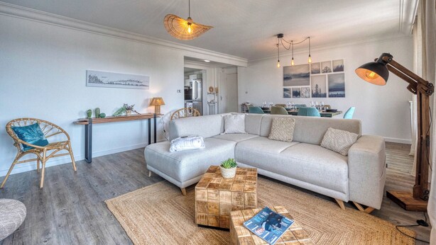 A modern living room with a grey sectional sofa, a wooden coffee table, and a dining area in the background.