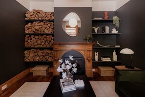 Een gezellige woonkamer met een open haard, boekenkasten en een spiegel boven de haardmantel.