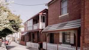 Une rangée de maisons de ville en briques, dotées de balcons, une clôture blanche en bois et une rue dégagée.
