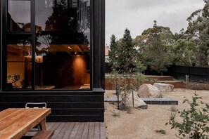 A modern building with large windows, a wooden deck, and a landscaped garden with rocks and trees. - 'Sisters' - Cliff top cabin with hot tub (Spring Beach)