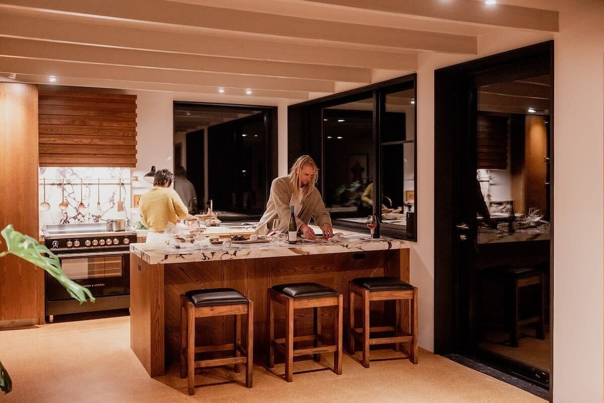 A modern kitchen with a central island, wooden stools, and a stove.