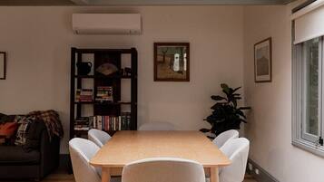 A dining area with a wooden table and four chairs, a bookshelf, a plant, and a window with blinds.