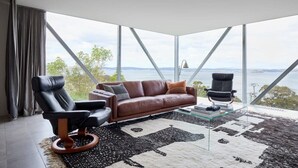 A modern living room with a leather sofa, two armchairs, and a glass coffee table. - Architectural Glass House with Breathtaking Ocean Views (Taroona)