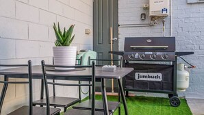 Une terrasse équipée d’un barbecue, de chaises, d’un pot de fleurs et d’un chauffage au gaz de marque Bosch.