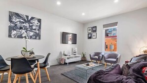 Un salon moderne avec un coin repas, une grande peinture abstraite et une vue sur un immeuble en briques.