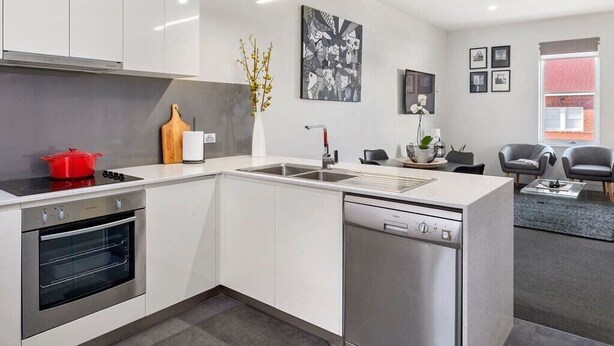Une cuisine moderne avec des meubles blancs, un four encastré, un lave-vaisselle et une casserole rouge sur la cuisinière.