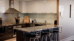 A modern kitchen with a central island, bar stools, stainless steel appliances, and a large range hood. - Fantastic CBD Apartment with Views (Hobart)