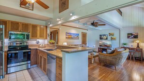 A spacious kitchen with wooden cabinets, a large island, and modern appliances. There is a dining area with a wicker chair and a small table.