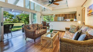 A spacious living area with wicker furniture, a glass coffee table, and a ceiling fan.